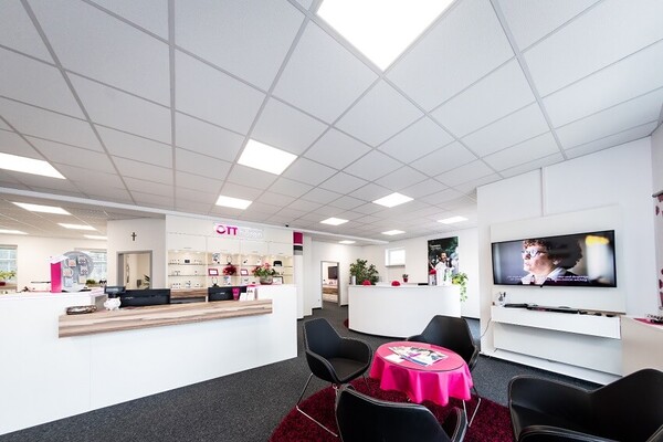 Modernes Hörakustik-Fachgeschäft mit Empfangstresen, Sitzbereich und Infobildschirm.